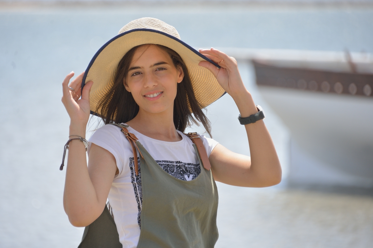Abir en chapeau devant une barque à Chergui, îles Kerkennah, Tunisie