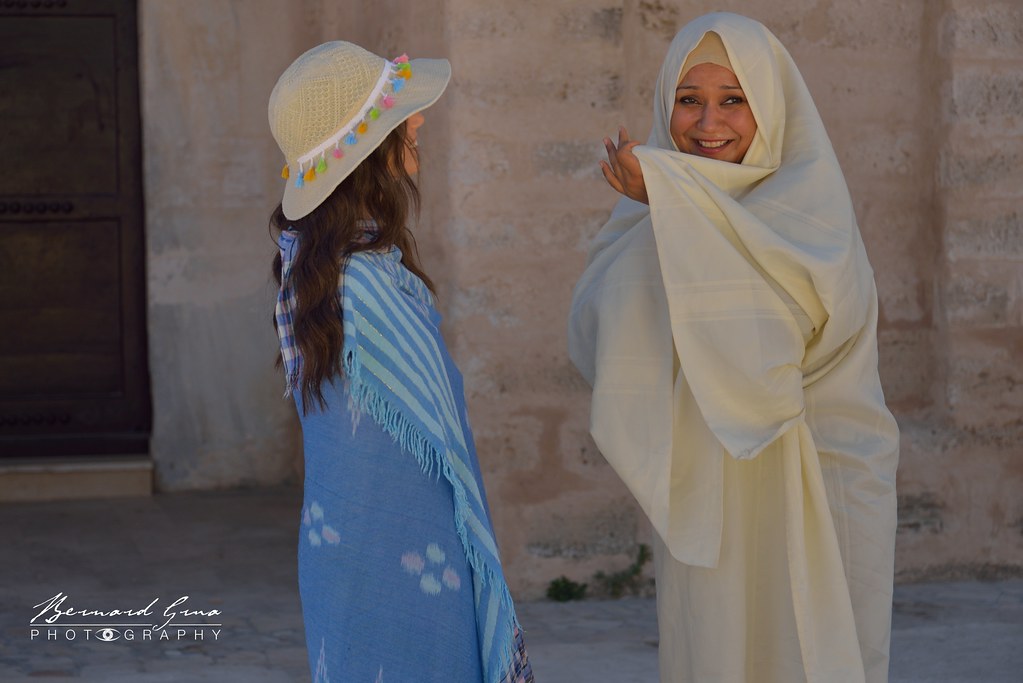 Deux femmes vêtues de tenues traditionnelles discutent devant un bâtiment de la médina de Mahdia.