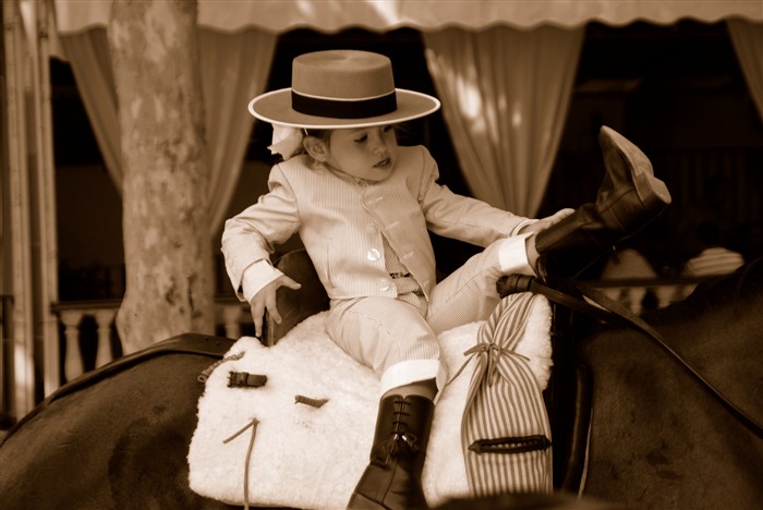 Petite fille en tenue équestre et chapeau andalou, assise sur un cheval pendant la feria d’Arcos de la Frontera.