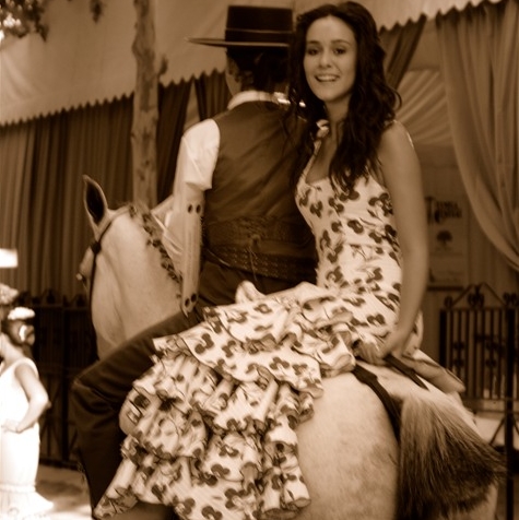 Jeune femme en robe andalouse à volants, assise en amazone sur un cheval pendant la feria d’Arcos de la Frontera. 