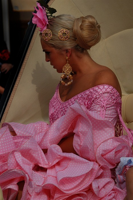Jeune femme en robe andalouse rose, assise dans un landeau et portant une fleur dans les cheveux à la Feria de Jerez de la Frontera.