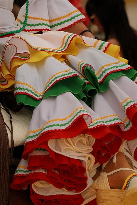 Détail d’une robe andalouse blanche à volants bordés de rouge, vert et jaune à la Feria de Jerez de la Frontera.