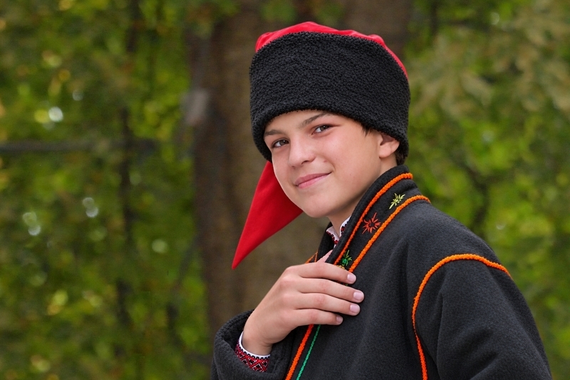 Jeune homme houtsoule portant une toque noire et rouge et un costume traditionnel sombre brodé.