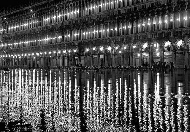 Place Saint-Marc à Venise pendant l'acqua alta, de nuit, avec les bâtiments et les reflets dans l'eau, en noir et blanc.