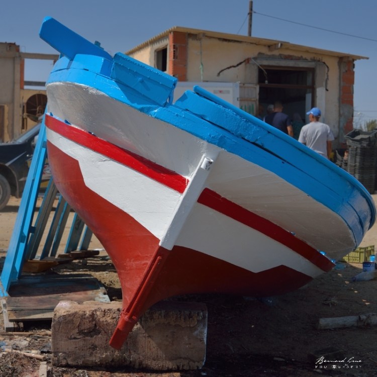 Bernard Grua - Poupe d'un loudso: sorties d'eau fines, arrière "canoé" et pavois arrondi débordant. Notez le bricolage popur la chaise du moteur hors-bord. A l'arrière babord la pièce de bois qui déborde est destinée à accueilir la "fourka" qui reçoit "l'antenne", vergue haute de la voile latine. El Attaya, Kerkennah, Tunisie, Chantier Naval Fathi Arous. 2 octobre 2019