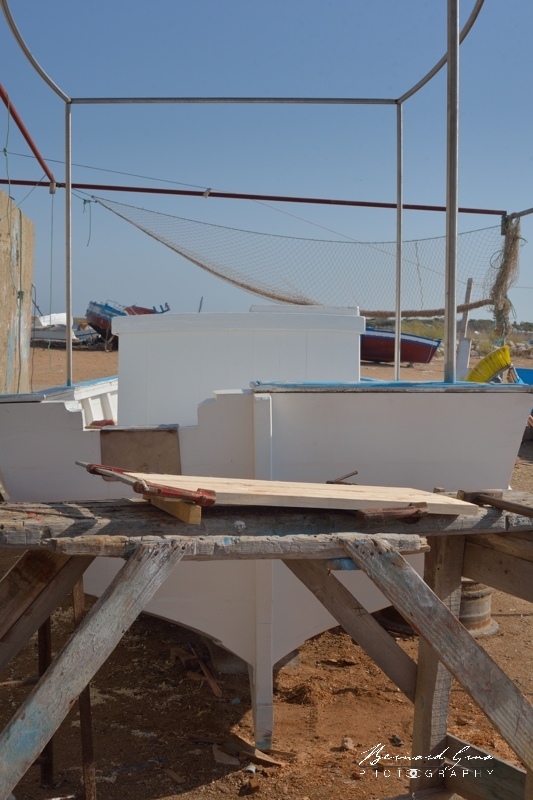 Il existe des floukas à moteurs in-bord. Ici, ce sera un hors bord. La structure verticale en inox a un double rôle. Elle sert à tendre un taud pour protéger le marin du soleil, puisqu'il ne peut plus jouir de l'ombre de la voile. La structure permet aussi de tendre des filets verticaux pour entasser sur le pont les drinas (nasses), maintenant en plastique, qui ont remplacé les gargoulettes en terre cuite utilisées pour piéger le poulpe. Chantier Naval Zouhir Chelly - El Attaya, Kerkennah, Tunisie. 2 octobre 2019