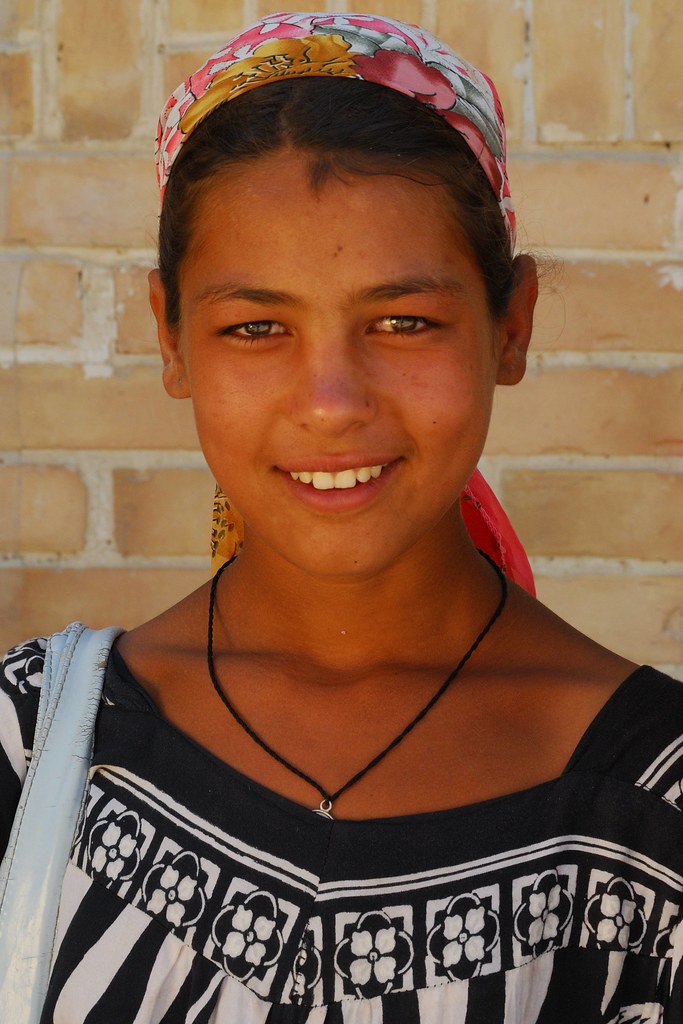 Jeune femme rom ouzbèke, portant un foulard coloré et une robe noire à motifs blancs, souriant devant l'objectif à Boukhara