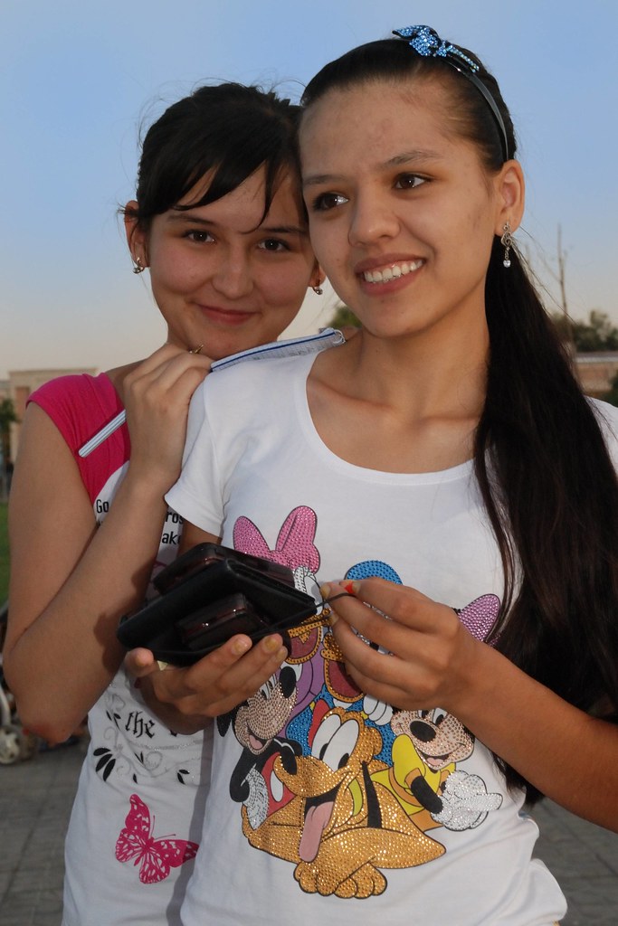 Deux jeunes femmes ouzbèkes posant ensemble, à Samarcande, l’une tenant un téléphone portable.